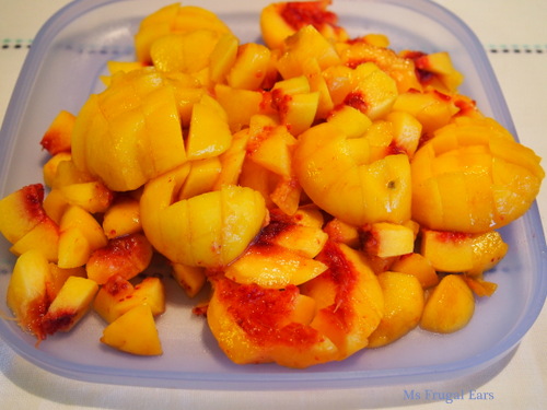 A pile of peaches sliced on a blue Tupperware plate